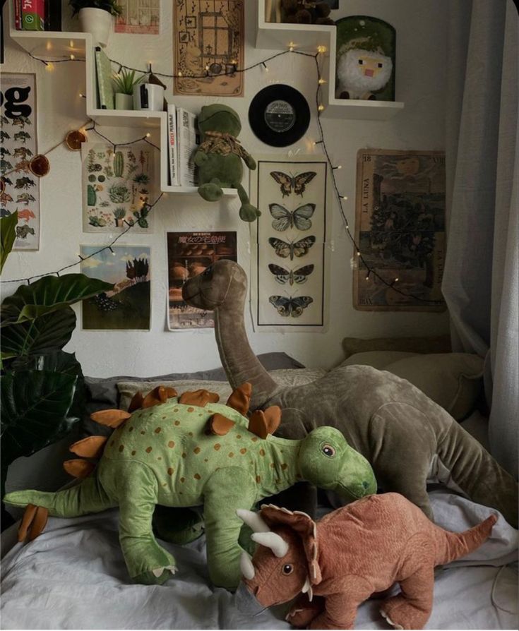 two stuffed dinosaurs sitting on top of a bed next to a wall full of pictures