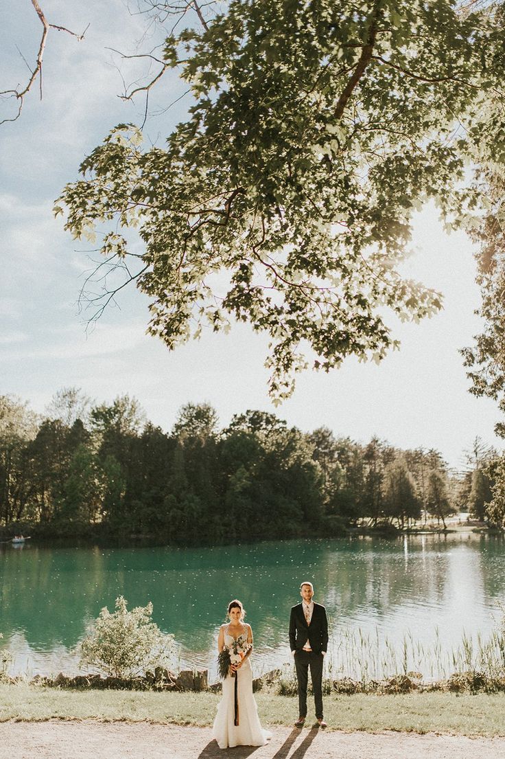 a bride and groom standing in front of a lake