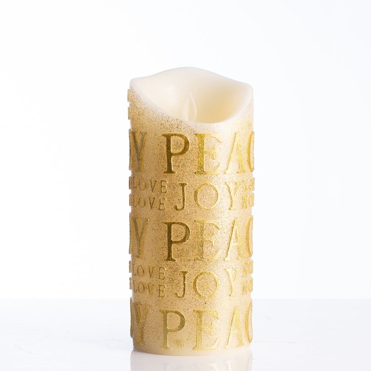 a white candle with gold lettering on it sitting on a table next to a wall