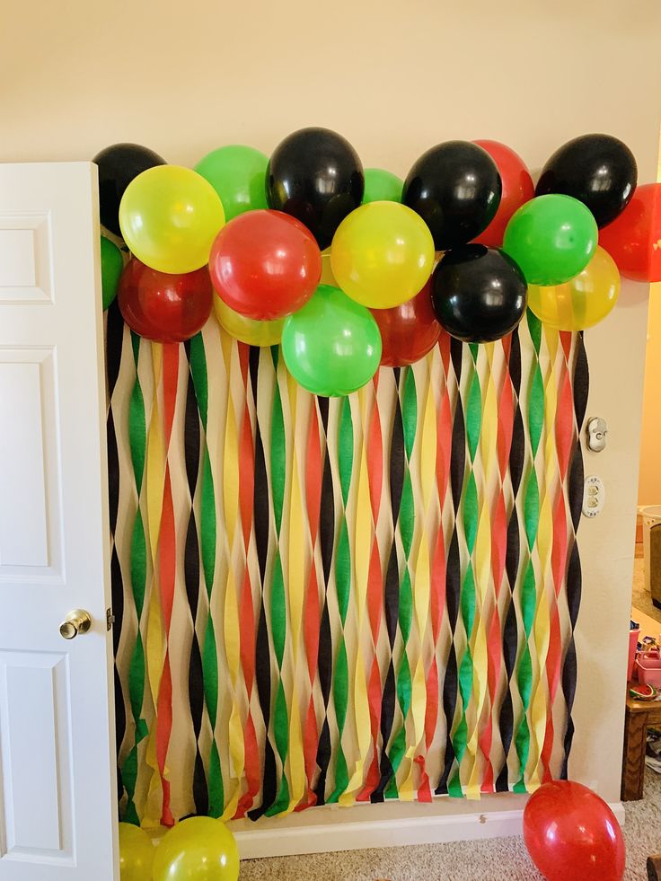 balloons and streamers are hanging on the wall in front of a party curtain with black, green, yellow, red, and orange stripes