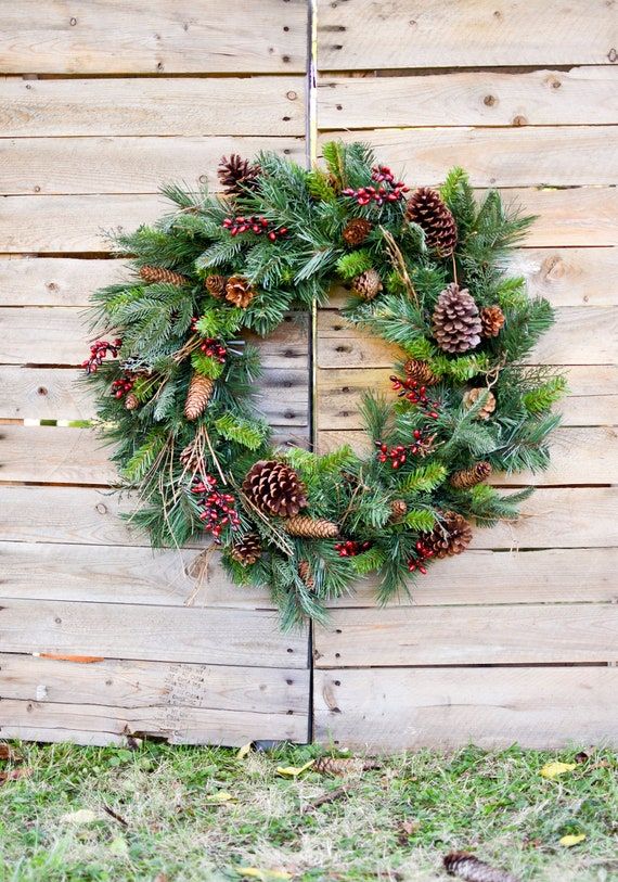 a christmas wreath hanging on the side of a wooden fence with pine cones and evergreens