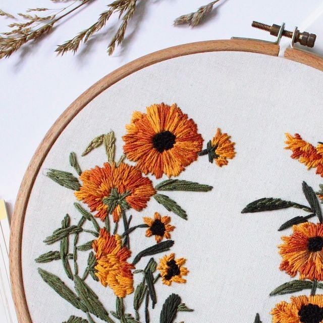 an embroidered hoop with orange flowers on it next to some scissors and threading needles