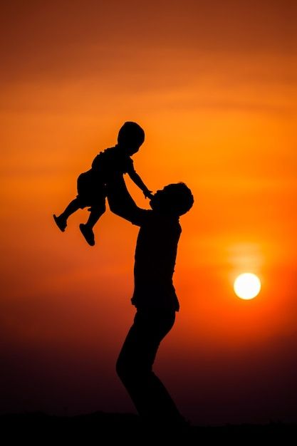 a man holding a child in his arms as the sun sets behind them with an orange sky