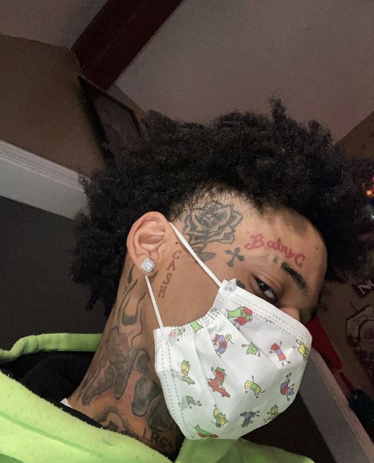 a young man wearing a face mask with tattoos on his neck and shoulder, looking at the camera