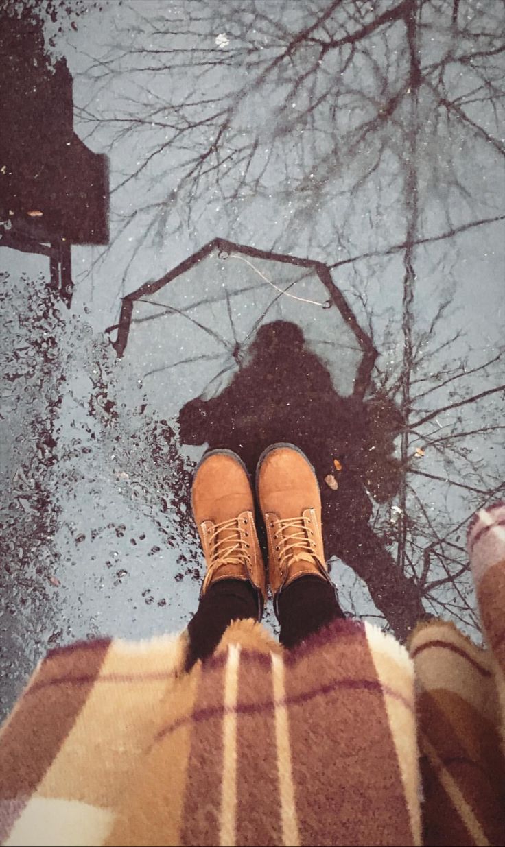 a person standing in the snow with their feet up and an umbrella reflected in the water