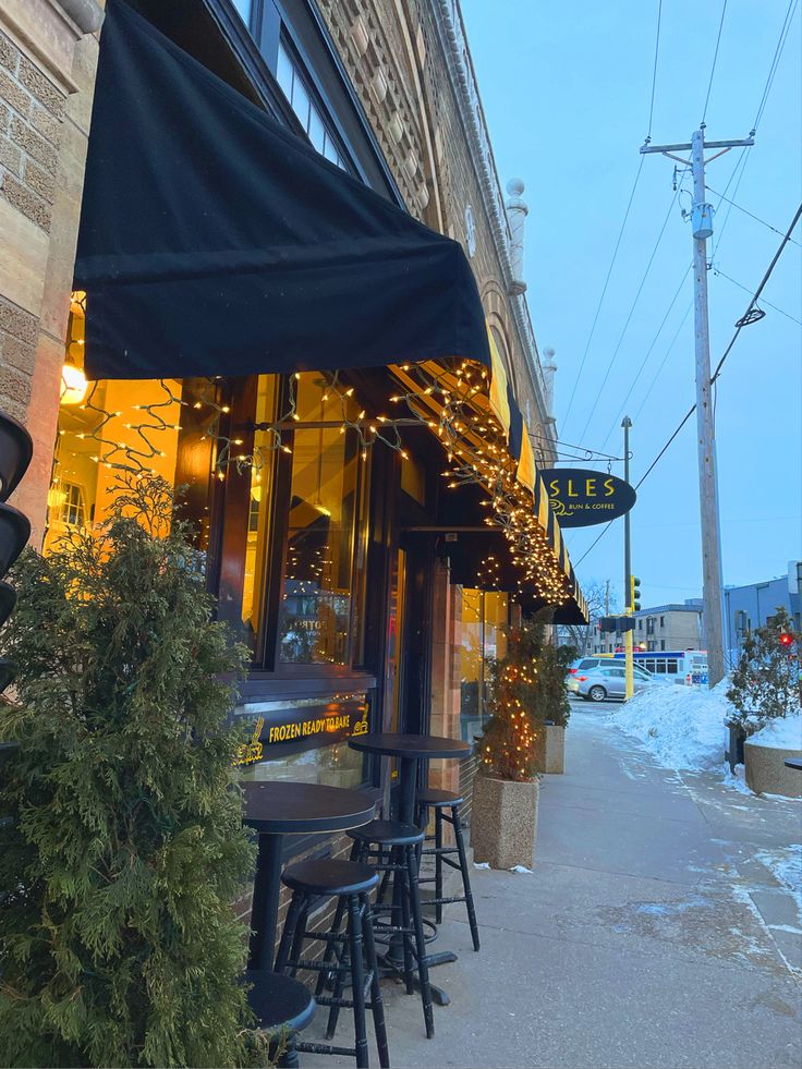 the outside of a restaurant with tables and chairs in front of it on a snowy day