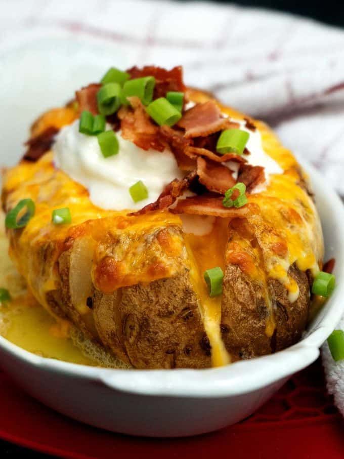 a baked potato with bacon and sour cream in a white bowl on a red plate