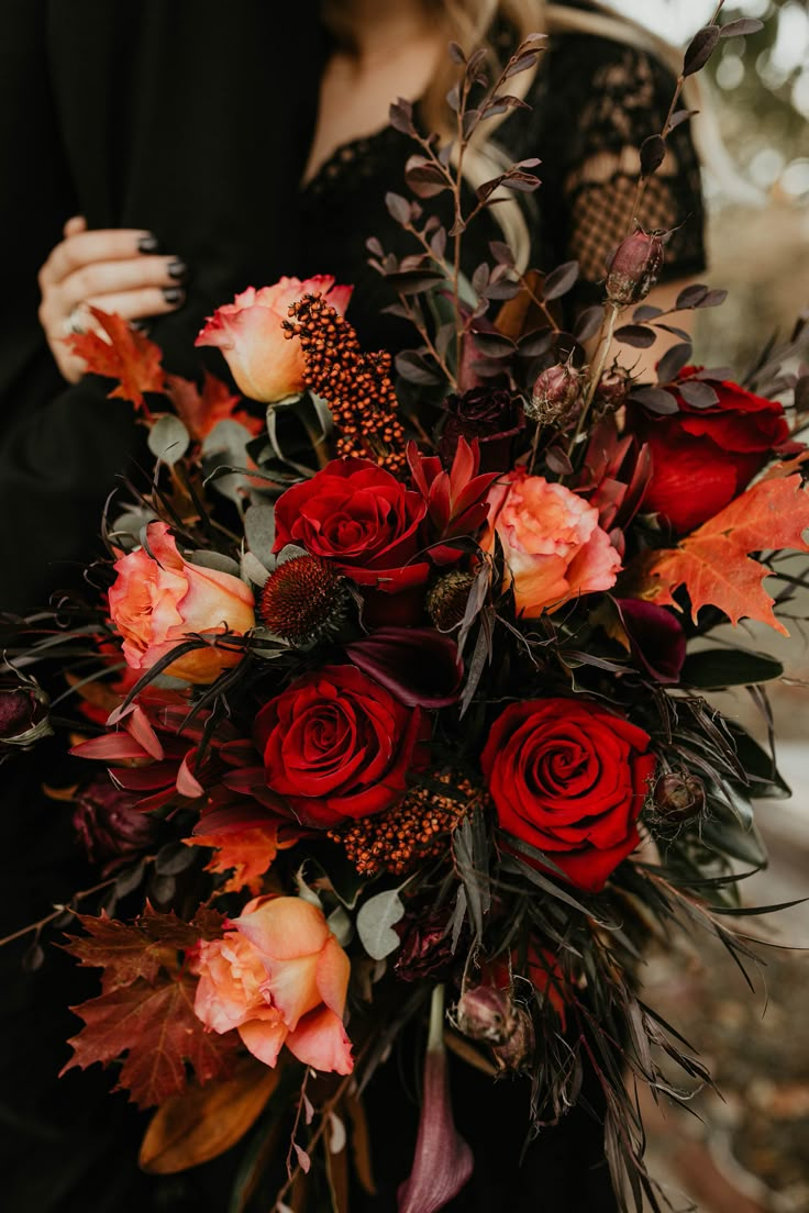 a woman holding a bouquet of red and orange flowers in her hands while standing next to a man