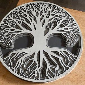 a metal plate with a tree cut out of it on a wooden table top next to a vase