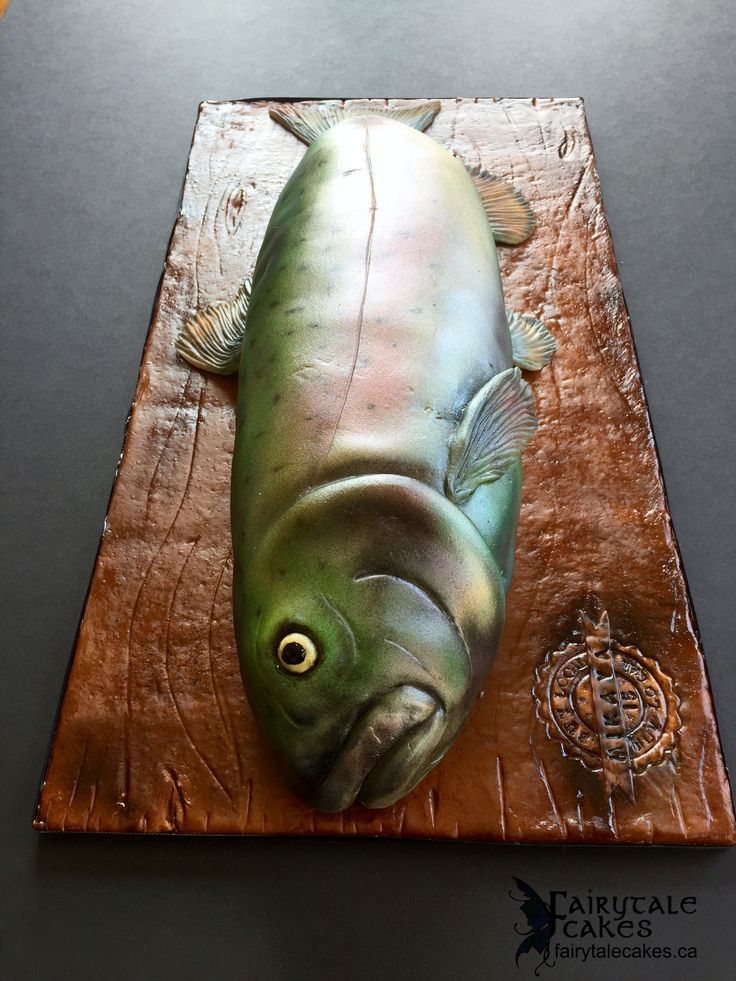 a fish shaped cake on top of a wooden cutting board, with the face of a fish carved into it's body