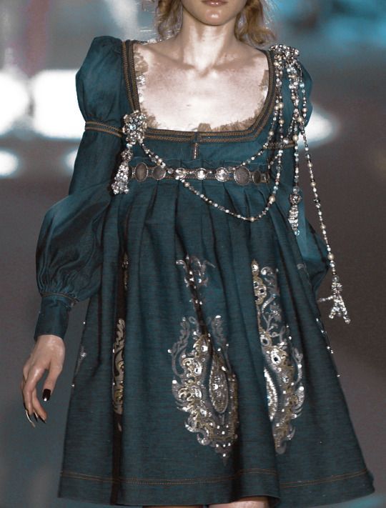 a woman walking down a runway wearing a green dress with chains on it's shoulders