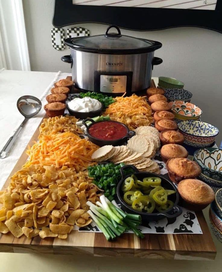 a wooden cutting board topped with different types of food next to a crock pot