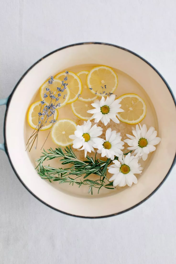 flowers and lemons are in a bowl with water on the side, along with herbs