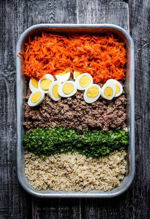 a tray filled with eggs, carrots and other food on top of a wooden table