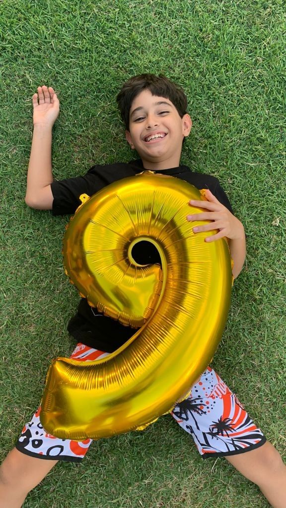 a young boy laying on the grass holding a giant number balloon