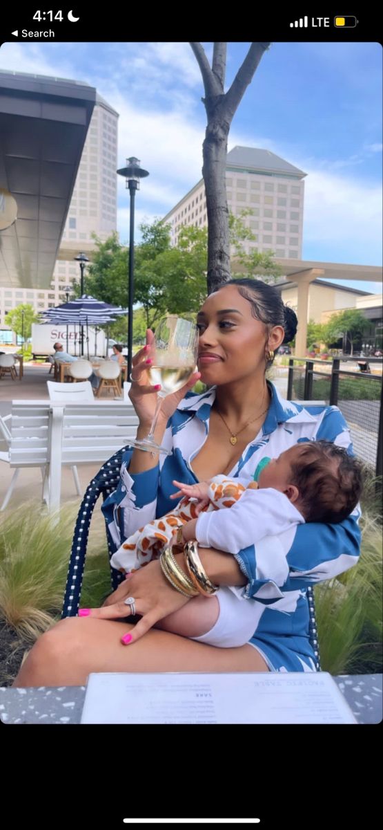 a woman holding a baby in her lap while sitting on a bench with buildings in the background