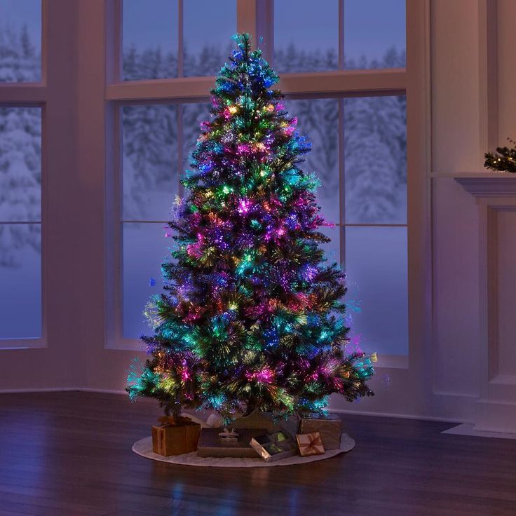 a brightly lit christmas tree sitting in front of a window on a hard wood floor