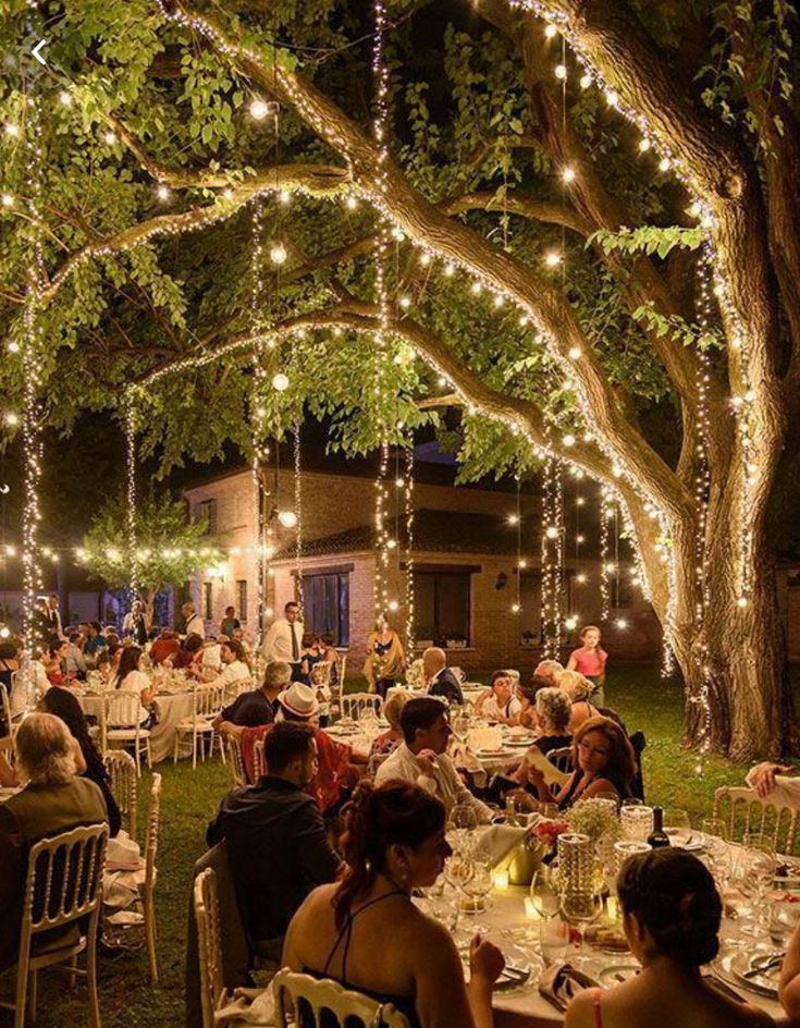 people are sitting at tables under trees with lights on them and the caption is in german