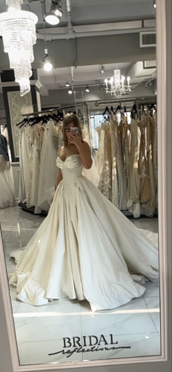 a woman standing in front of a mirror wearing a wedding dress and looking at her cell phone