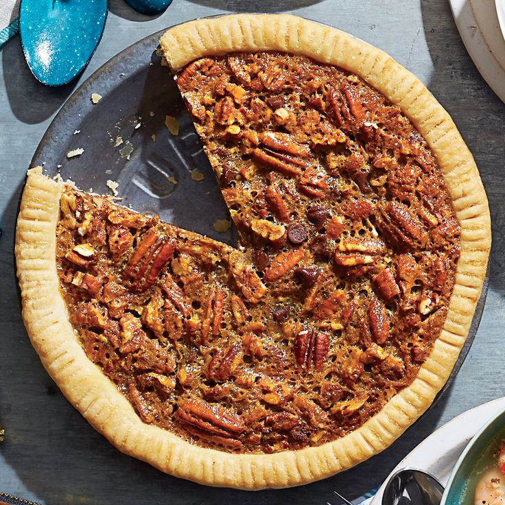 a pecan pie with one slice missing from it on a table next to plates and utensils