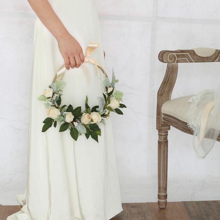 a woman in a white dress holding a basket with flowers on it next to a chair