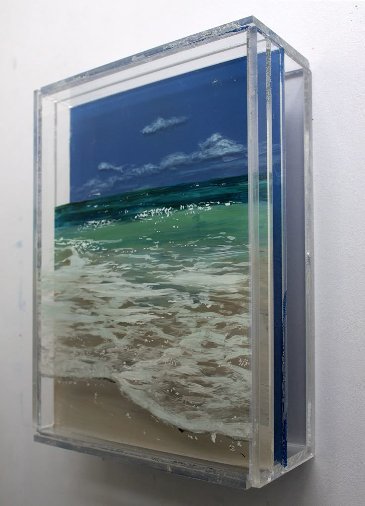 a glass block hanging on the side of a wall with water and clouds in it