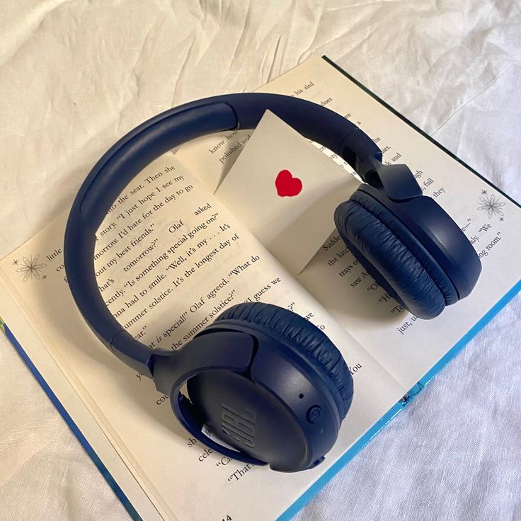 an open book with headphones laying on top of it next to a pair of blue headphones