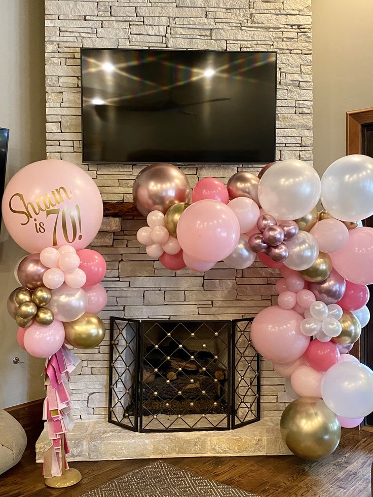 the balloon arch is decorated with pink, gold and white balloons in front of a brick fireplace