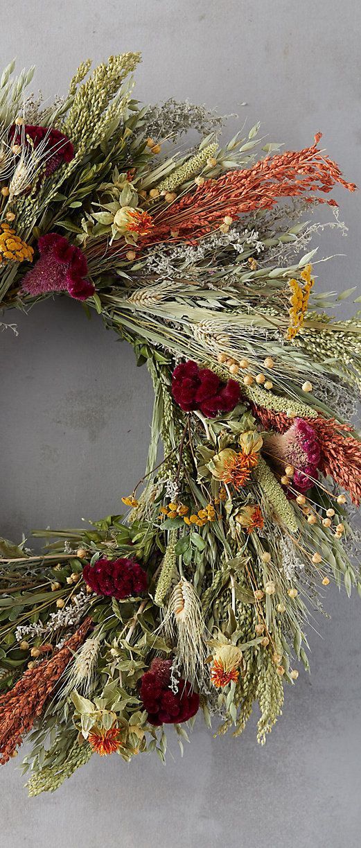 a wreath with dried flowers and grass on it is shown in front of a gray background