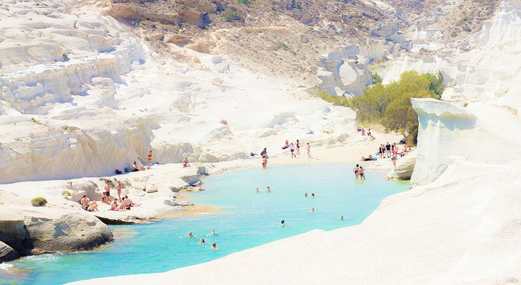 many people are swimming in the water near some rocks and sand, while others stand around them