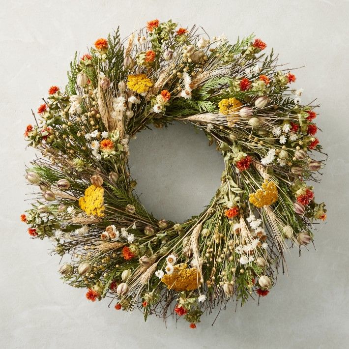 a wreath made out of dried flowers and grass on a white background with orange, yellow, and red berries