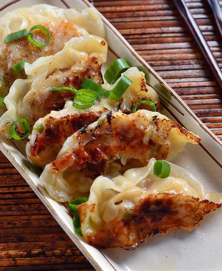 a white plate topped with dumplings covered in sauce and green onions on top of a wooden table