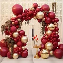 two red and gold christmas decorations in front of a white wall with an arch made out of balloons