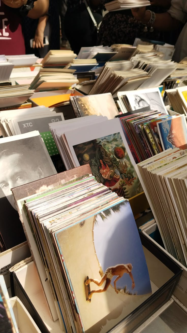 many books are stacked on top of each other with people in the background looking at them