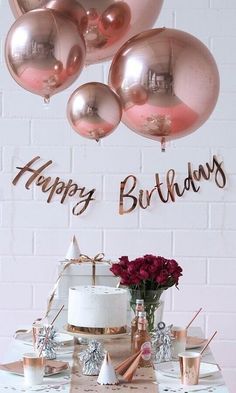 a table topped with lots of pink and gold balloons next to a white brick wall