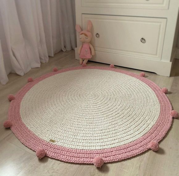 a pink and white round rug with pom - poms on the floor next to a dresser