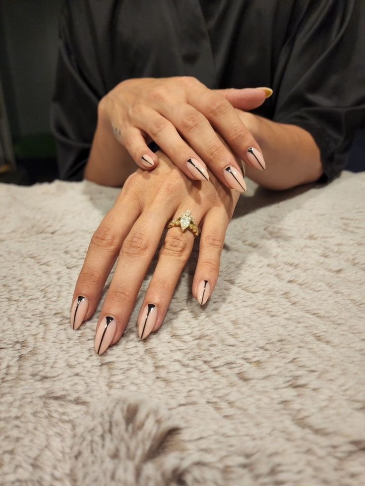 Two relaxed hands, one over the other, palms down to display light pink/nude colored stilleto shaped nails with straight black line detail from tip to cuticle. Light tan fur background. Black Line Manicure, Black Triangle Nails, Vertical Line Nails, Black Fine Line Nail Art, Minimalist Nails Almond Fall, Black Lined Nails, Nails With Straight Lines, Minimal Line Nails, Black Lines Nail Art