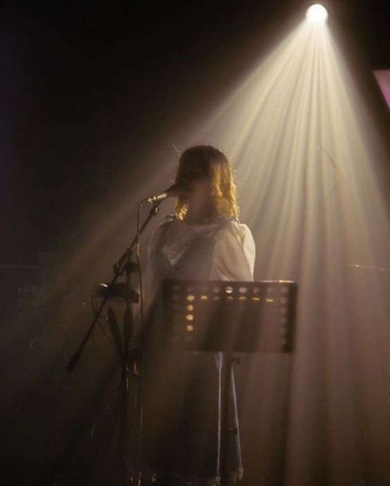 a woman standing in front of a microphone on top of a keyboard under a spotlight