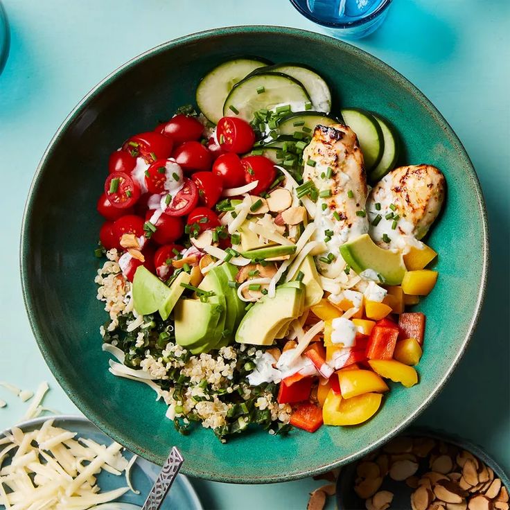 a blue bowl filled with chicken, vegetables and rice next to sliced cucumbers