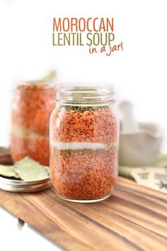 two jars filled with red lentils sitting on top of a wooden table next to a spoon