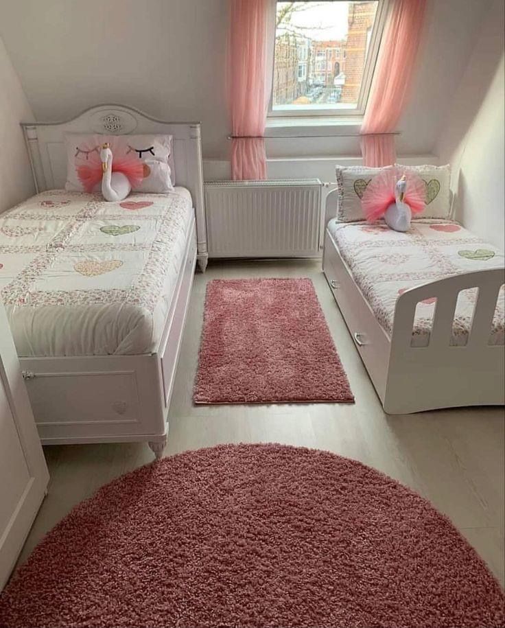 two twin beds in a small room with pink rugs on the floor and windows