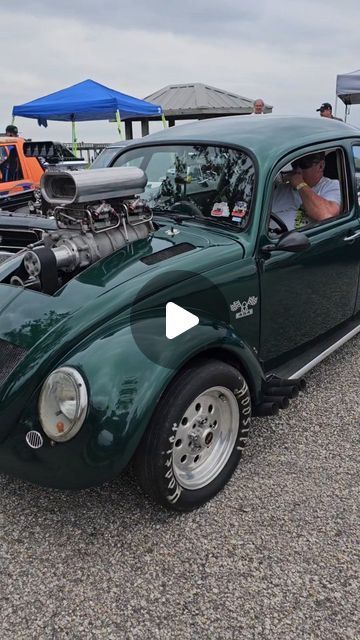 a green vw bug parked next to other cars in a parking lot with people looking at it