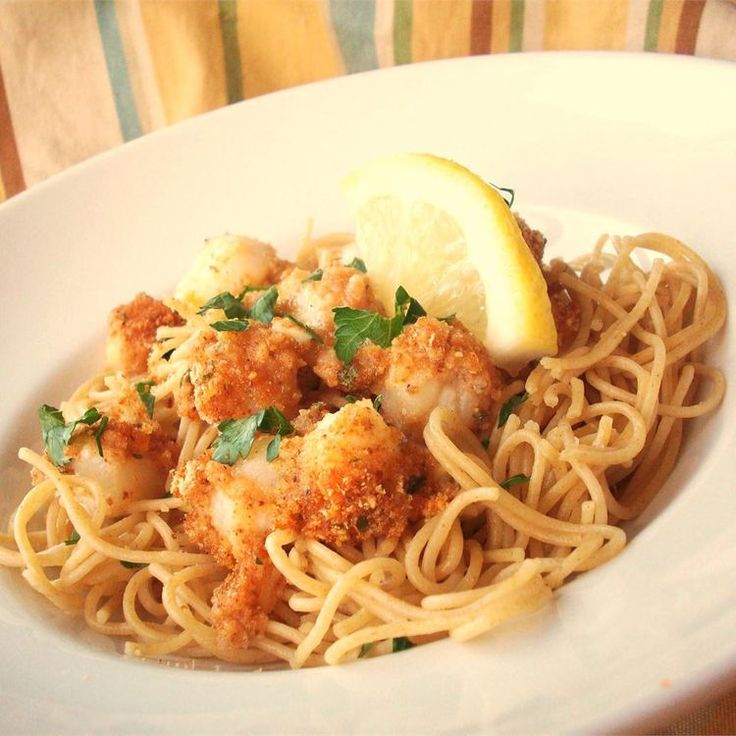 a white plate topped with pasta covered in sauce and meat next to a lemon wedge