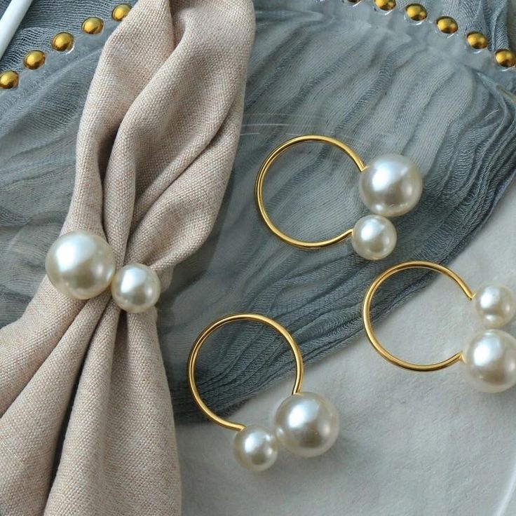 three pairs of pearl earrings sitting on top of a white cloth next to a pair of gold hoop earrings