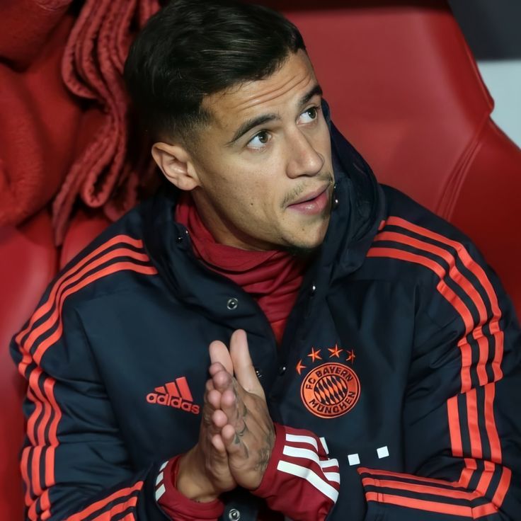 a soccer player sitting in the dugout with his hands folded and looking at something