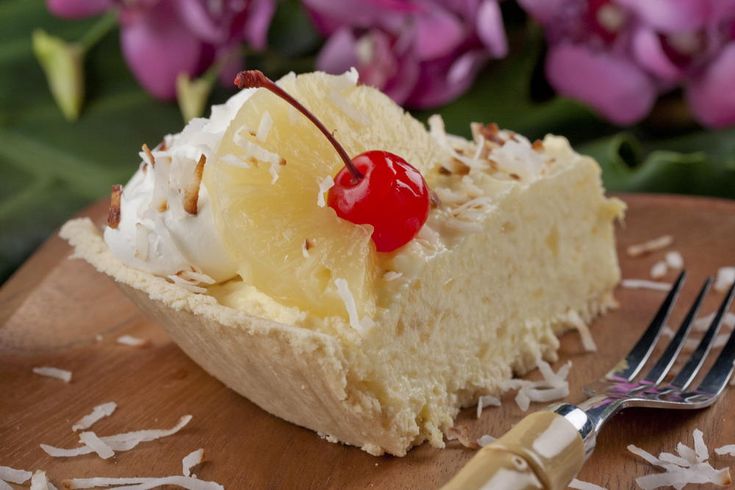 a piece of cake on a wooden plate with a fork and purple flowers in the background