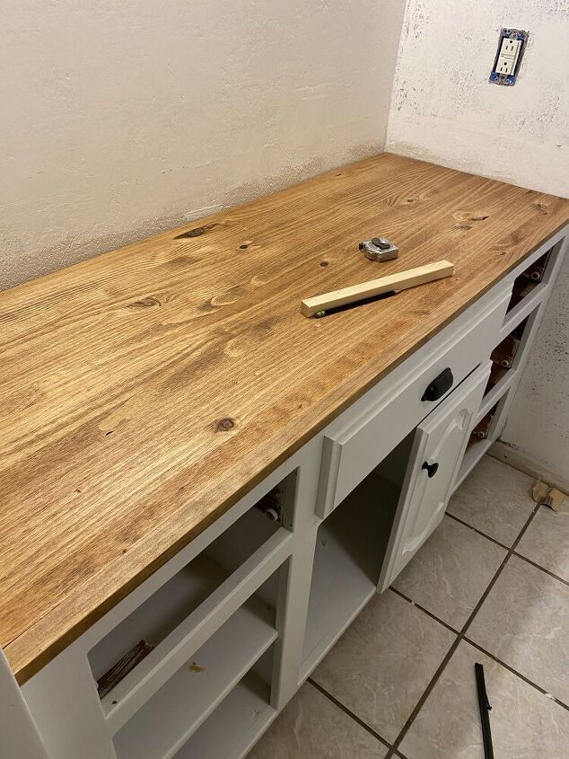 a wooden counter top sitting on top of a white cabinet next to a wall with tools