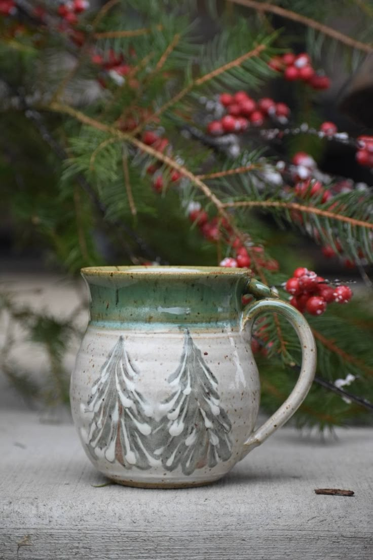 a white and green mug sitting on top of a table next to a pine tree