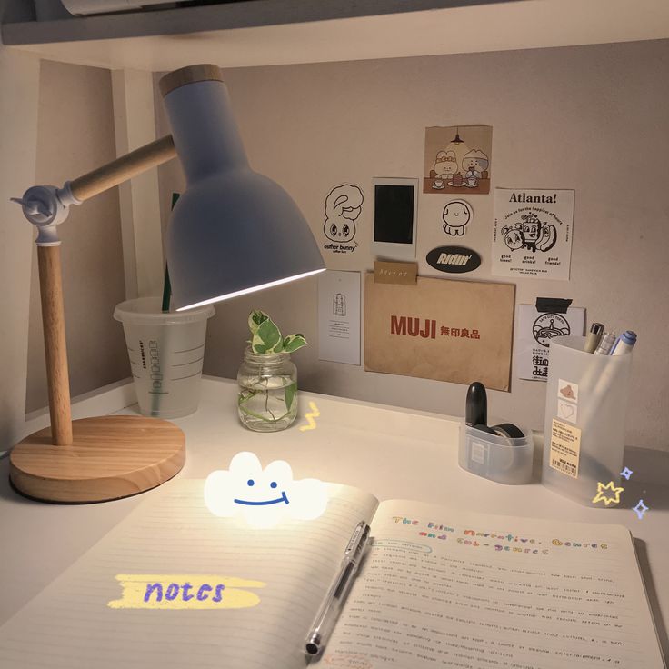 an open notebook sitting on top of a desk next to a lamp