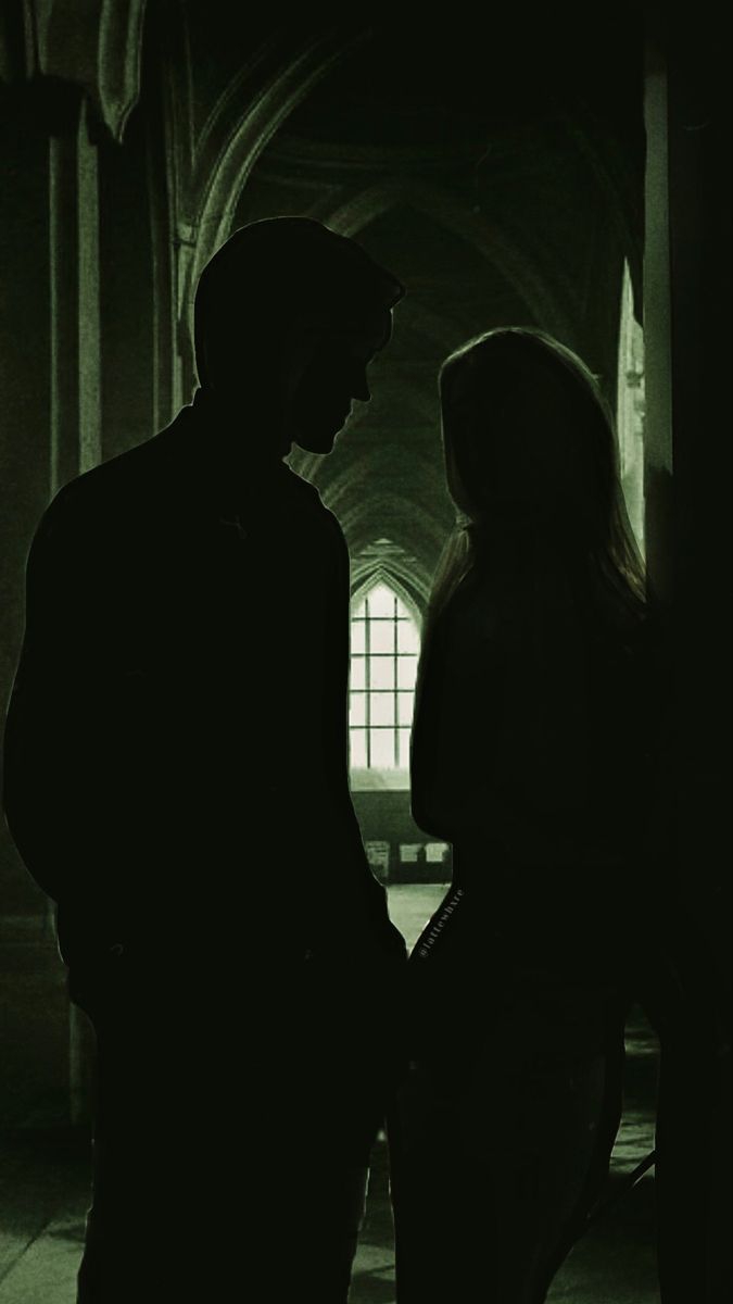 a man and woman standing next to each other in a dark room with light coming through the window